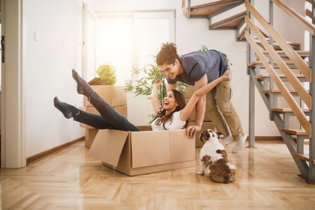 A couple and their pet in their new house full of empty cardboard boxes